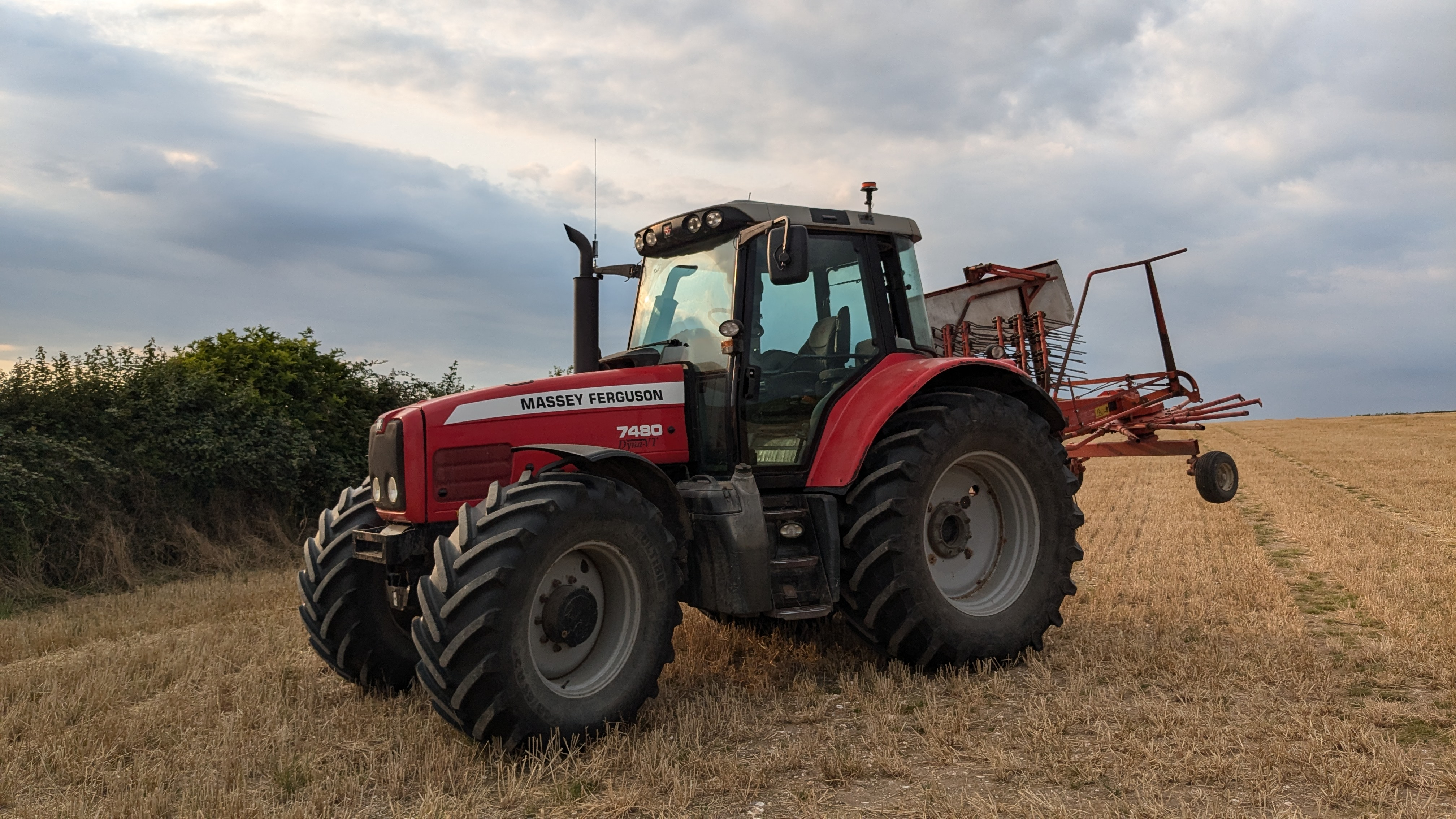 A massey Ferguson tractor in a field, fitted with a hay rake